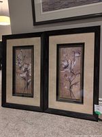 Both framed floral prints standing side by side on carpet