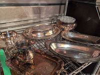 Overview of all silverplate serveware pieces and vase with glass frog on shelf