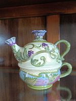 Side view of stacked teapot on cup showing hand-painted vine and grape motif