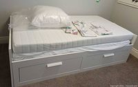 assembled white Ikea daybed with mattress, pillow form and folded sheet set on top
