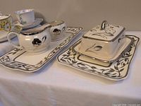 Full set showing cream pitcher, sugar bowl on large tray and lidded butter keeper on small tray