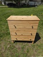 Front view of natural pine three-drawer dresser on grass