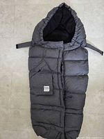 Front view of gray hooded stroller footmuff showing logo patch, quilting, zipper and side straps