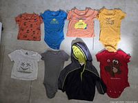 Eight baby clothing items laid out: six onesies, one t-shirt, one hoodie