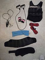 All items laid out: weighted vest, resistance tube, gloves, jump rope, ankle weights, towel/heat pack, lumbar belt