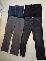 Overview of four pairs of men’s pants laid flat: blue jeans, black jeans, gray cargo, charcoal jeans