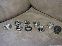 All nine blackened metal rings laid out on fabric surface showing front and top motifs