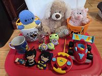 Overview of full lot on red tray showing plushes, RC car, remote, mug, buckets, rattles, die-cast car