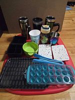All items laid out including travel mugs, bottle, mugs, bowl, molds, tray, tongs and coasters