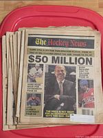 Stack of The Hockey News newspapers on red surface, top issue headline "$50 MILLION"