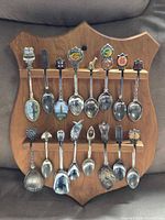 Full view of 19 souvenir spoons on wooden shield plaque