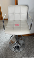 Front view of white tufted faux leather swivel bar stool with chrome pedestal and footrest