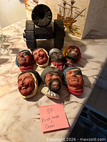 Group view of seven pirate head plaques and model cannon