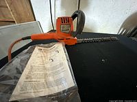 Black & Decker orange hedge trimmer with attached cord and user manual on table