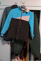 Blue, black and grey May West coat hung front, dark green coat and green quilted pants visible