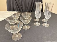 Five coupe glasses and four Longchamp flutes displayed on a black surface