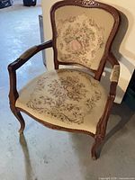 Front three-quarter view of carved wooden armchair with needlework upholstery
