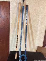 Three Cooper ringette sticks and blue ring leaning against wall