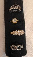All four rings on black display: braided silver puzzle ring, floral ring, cluster ring, infinity ring