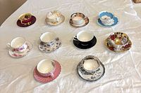 Ten assorted teacup and saucer sets laid out on cloth