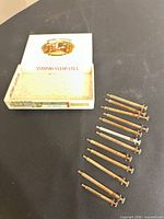 Open Antonio y Cleopatra cigar box beside row of glass syringes