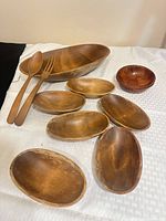 Large oval bowl, six oval side bowls, one round bowl, wooden fork and spoon displayed on cloth