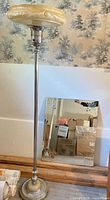 Full view of chrome floor lamp with cream torchiere shade and etched rectangular mirror leaning against wall