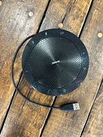 Top view of black Jabra circular speakerphone with control icons and attached USB-A cable