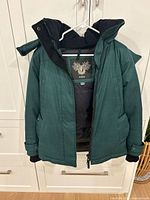 Front view of dark green Nobis parka showing zipper, storm flap, pockets and cuffs