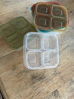 Stack of six square plastic containers with four compartments shown with assorted colored lids