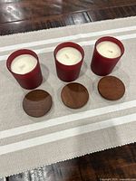 Top view of three burgundy glass candles with lids removed, showing white wax and wicks