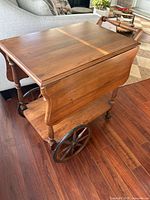 Angle view of solid wood tea cart showing drop-leaf side down, lower shelf, large spoked wheel