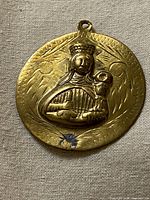 front of round gold-tone medallion showing crowned figure and child relief
