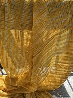 Full view of sheer yellow striped curtain hanging over railing in sunlight