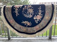 Full view of half-folded round rug over railing showing overall design and fringe