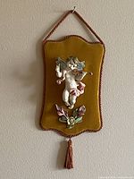 Front view of porcelain cherub wall plaque on velvet board with tassel