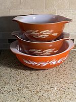 Three stacked orange Pyrex bowls showing wheat design and white interiors