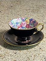 Cup on saucer showing black exterior, gold rim, floral interior