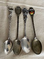 Front view of all four sterling souvenir spoons showing handle motifs and bowl condition