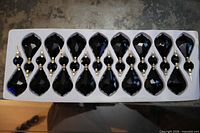 Tray holding sixteen black faceted drop crystals with connectors