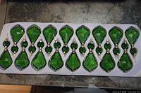 Tray holding sixteen emerald green glass drop prisms with round connector beads and gold-tone pins