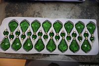 Tray holding 16 faceted emerald green chandelier drops