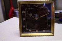 front view of square brass-framed clock showing dial and hands