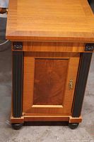 Front view of bedside table showing door, fluted accents, brass pull, and chipped bottom trim