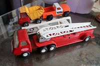 All five Tonka pieces: red cab attached to fire-truck body with ladder extended, white car-hauler trailer with yellow dump and orange pickup