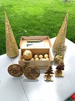 Group view showing two gold cone trees, open box of ornaments, sleigh, plates, candleholders