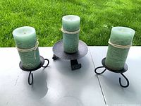 Three black metal candle holders with green pillar candles on a table outdoors