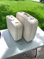 Two ivory hard shell suitcases side by side on table
