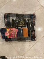 Sealed plaid polar fleece throw blanket with additional packaged socks visible