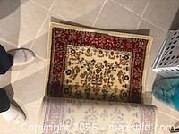 Rug partially unrolled showing ivory field with floral motifs and red border